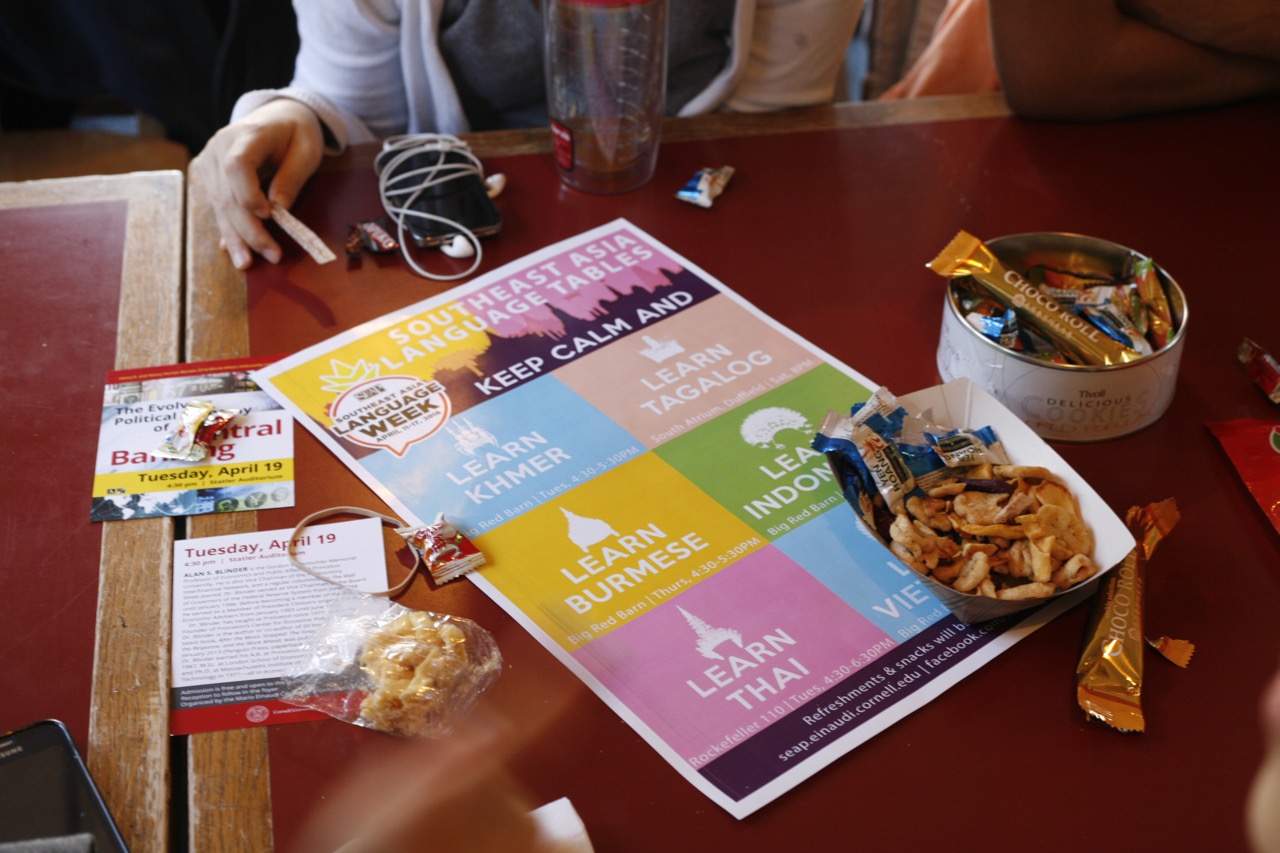 A flyer listing the six Southeast Asian languages taught at Cornell, placed on a table and surrounded by Southeast Asian snacks