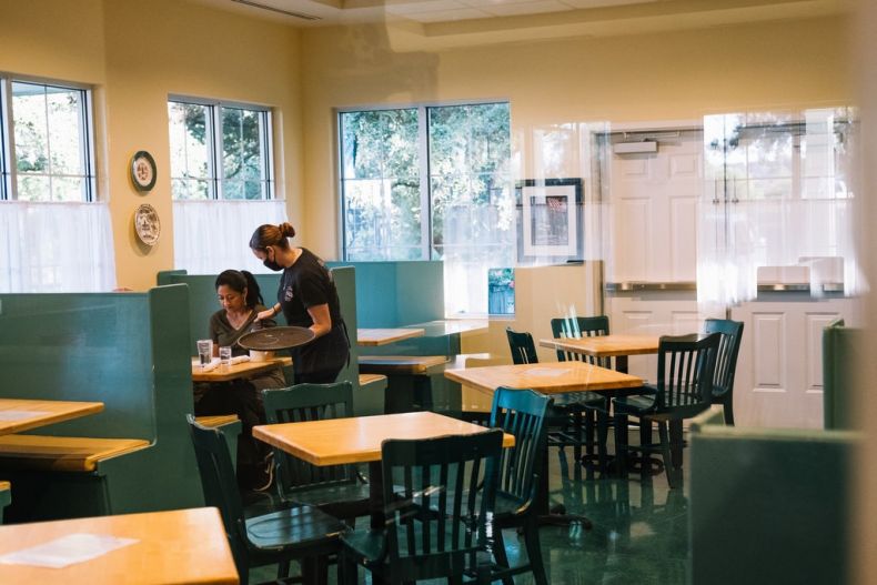 Waitress wearing mask serves customer in empty restaurant