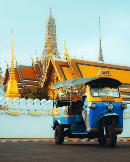 A blue and yellow auto rickshaw in Thailand, in front of the Grand Palace.