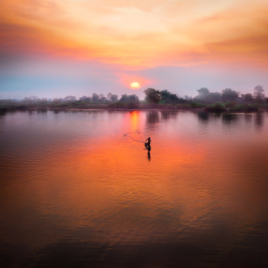 A man fishing on a boat at sunset.