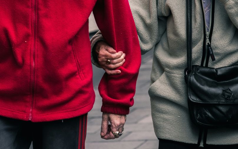 Two people with wrinkled hands link arms.