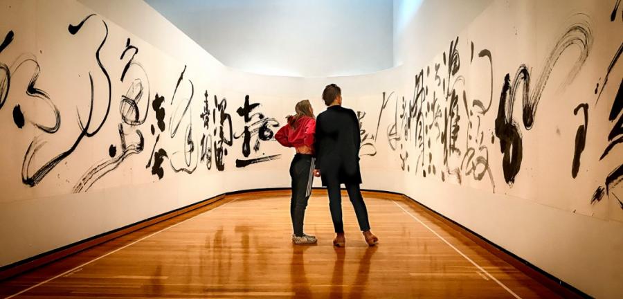 Two people standing in a gallery with calligraphic art on the surrounding walls