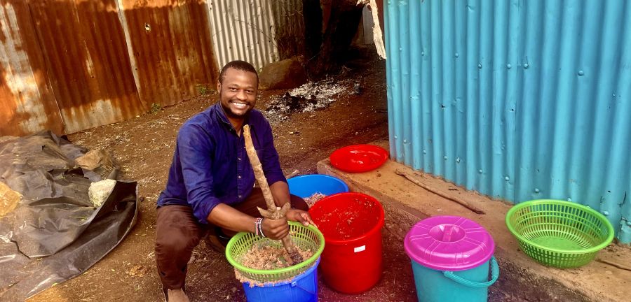Jensen Njagi squats down next to colorful buckets. 