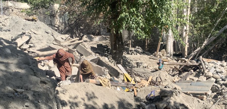 Two women climb up rocks and rubble after a flood caused destruction.