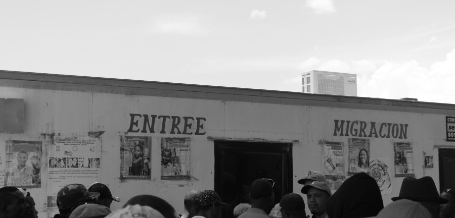 A crowd stands around a building that reads "Entree Migracion." 