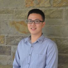 Chuling smiles wearing glasses and light blue shirt against a stone facade