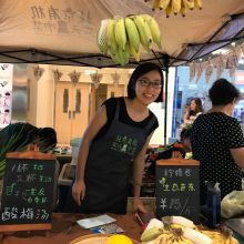 Miamiao stands over a table of food and smiles towards camera