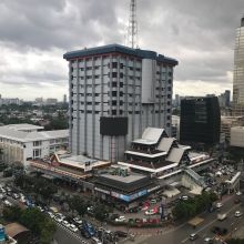 A tall gray building stands amidst a complex of other buildings with a gray sky overhead