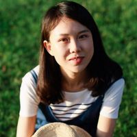 Yuanyuan sits on the grass, arms wrapped around her knees shoulder length hair white and navy striped top and denim jumper