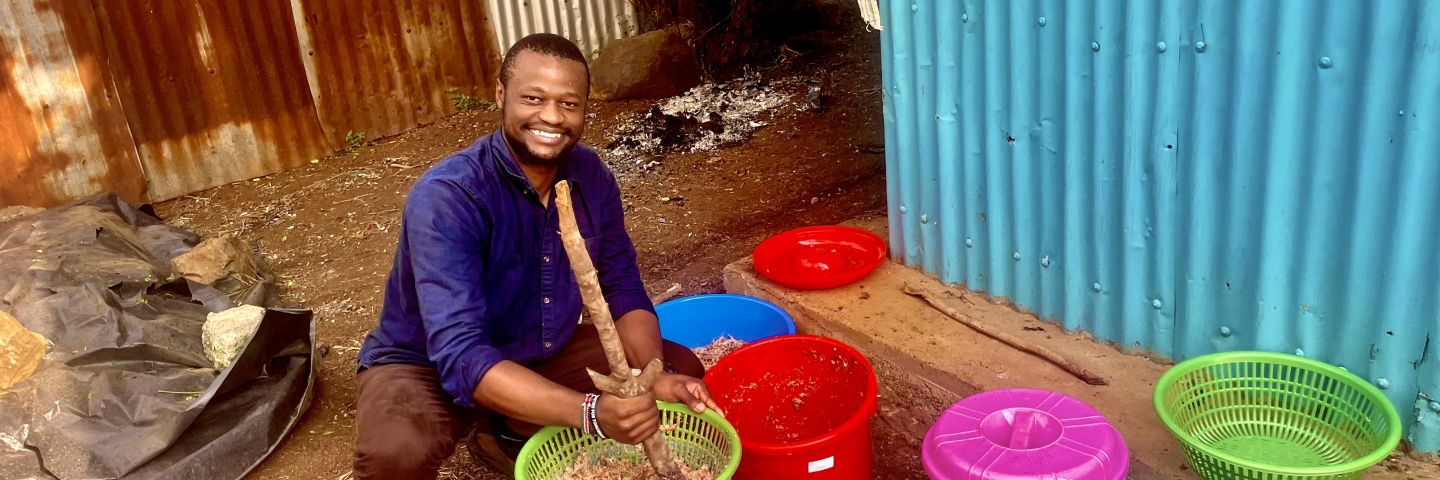 Jensen Njagi squats down next to colorful buckets. 