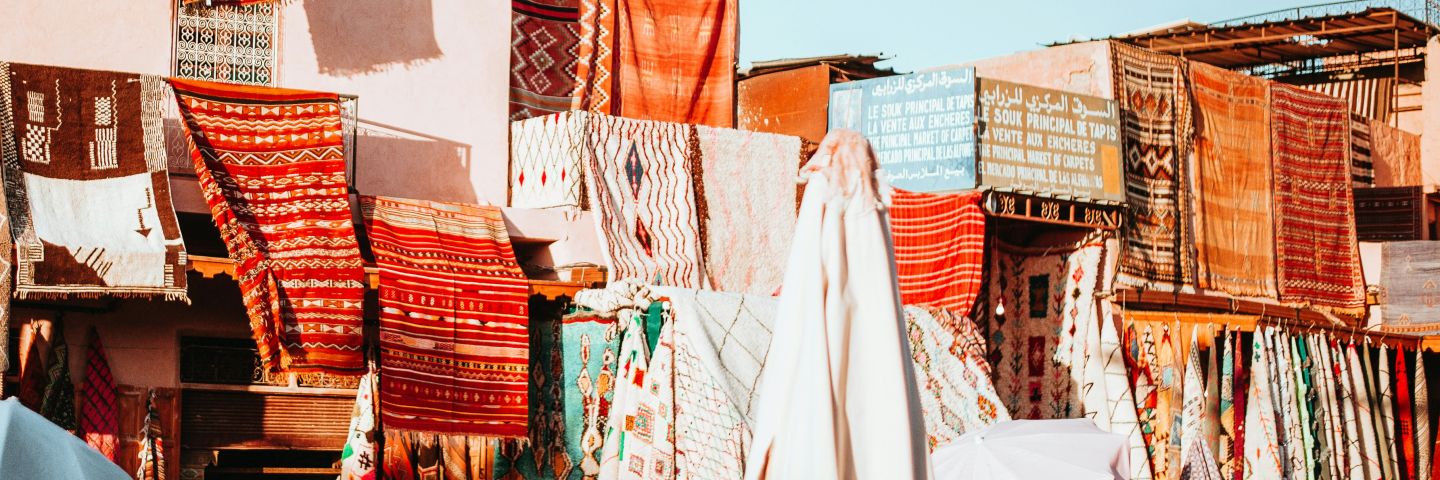 Bright orange and red rugs hang over buildings in Marrakesh.