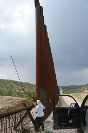 Humanitarian patrollers drive up to an opening between fence and border wall.