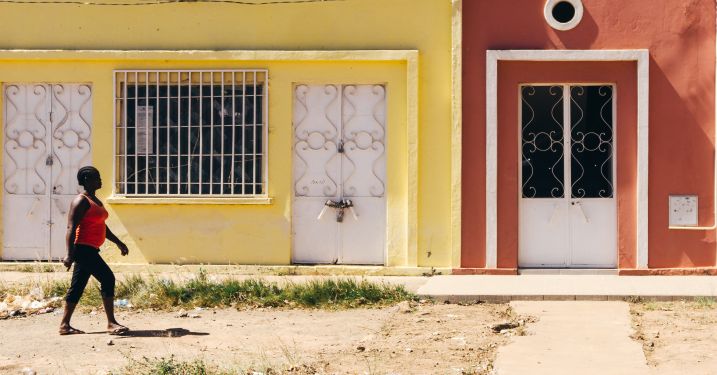 A person walks past yellow and red buildings.