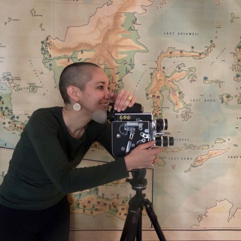 Emiko Stock with a camera at the Kahin Center in front of a map of Indonesia