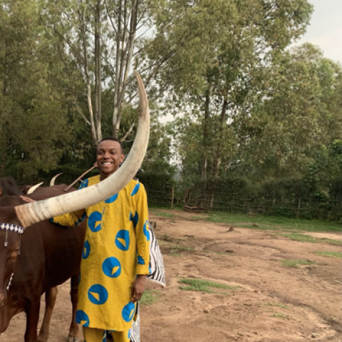 Aliou Jabari Gambrel wears traditional African dress and stands near a bull