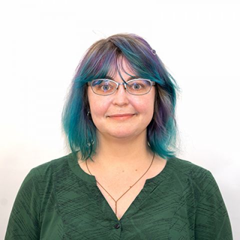 Photo of Alexis Siemon. Wearing a green blouse, with blue and purple highlighted hair, and wearing glasses.