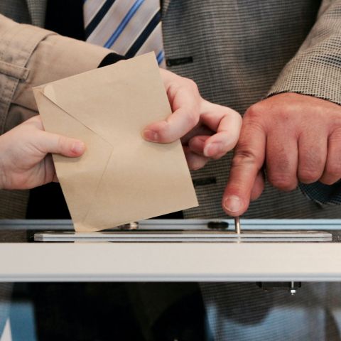 Hands holding placing a voting ballot into a receptacle.