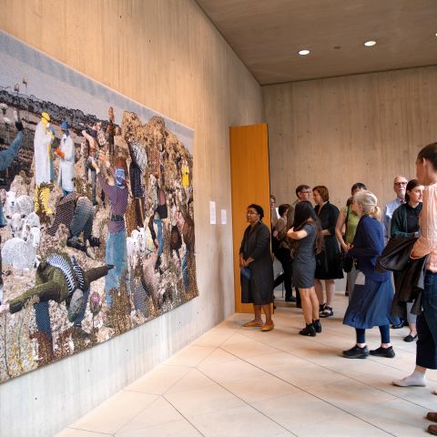 An audience looks at a large woven piece of art hanging in the Johnson Museum