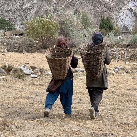 Two women walk along a dirt path carrying woven baskets