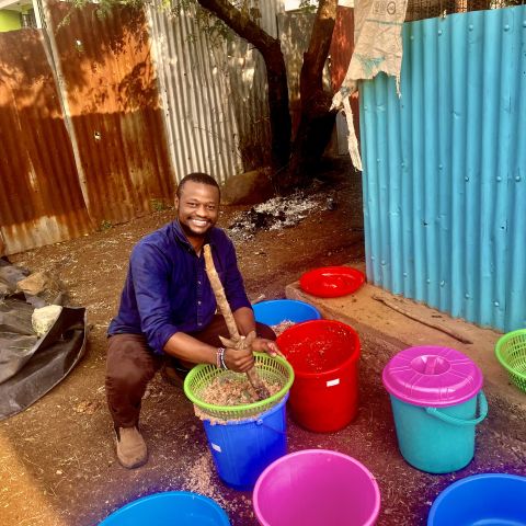 Jensen Njagi squats down next to colorful buckets. 