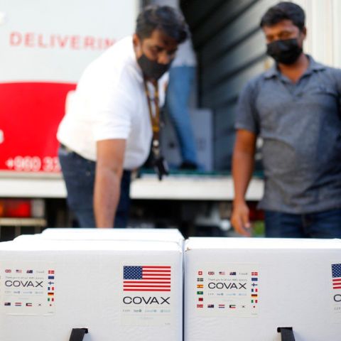 Two masked men stand over boxes of vaccines. 