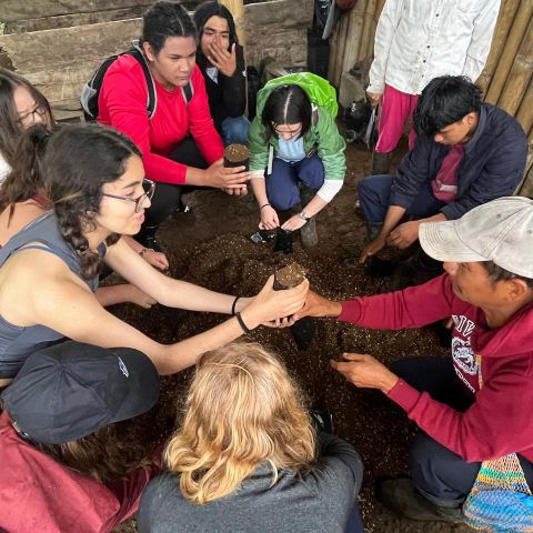 Laidlaw scholar hands a clump of a soil to an Ecuadorian man.