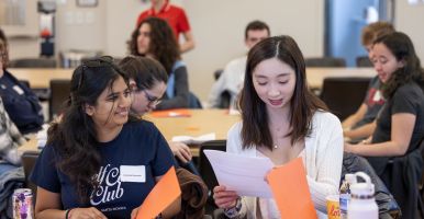 Laidlaw scholars work together on a leadership activity while seated and looking through orange folders.